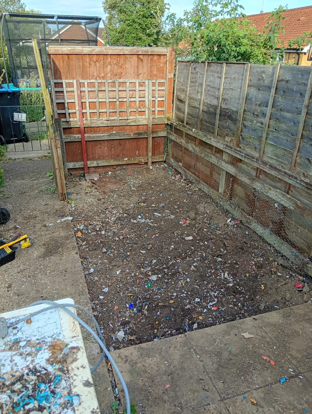 The same garden corner cleared to bare soil, fence panels and paving visible again