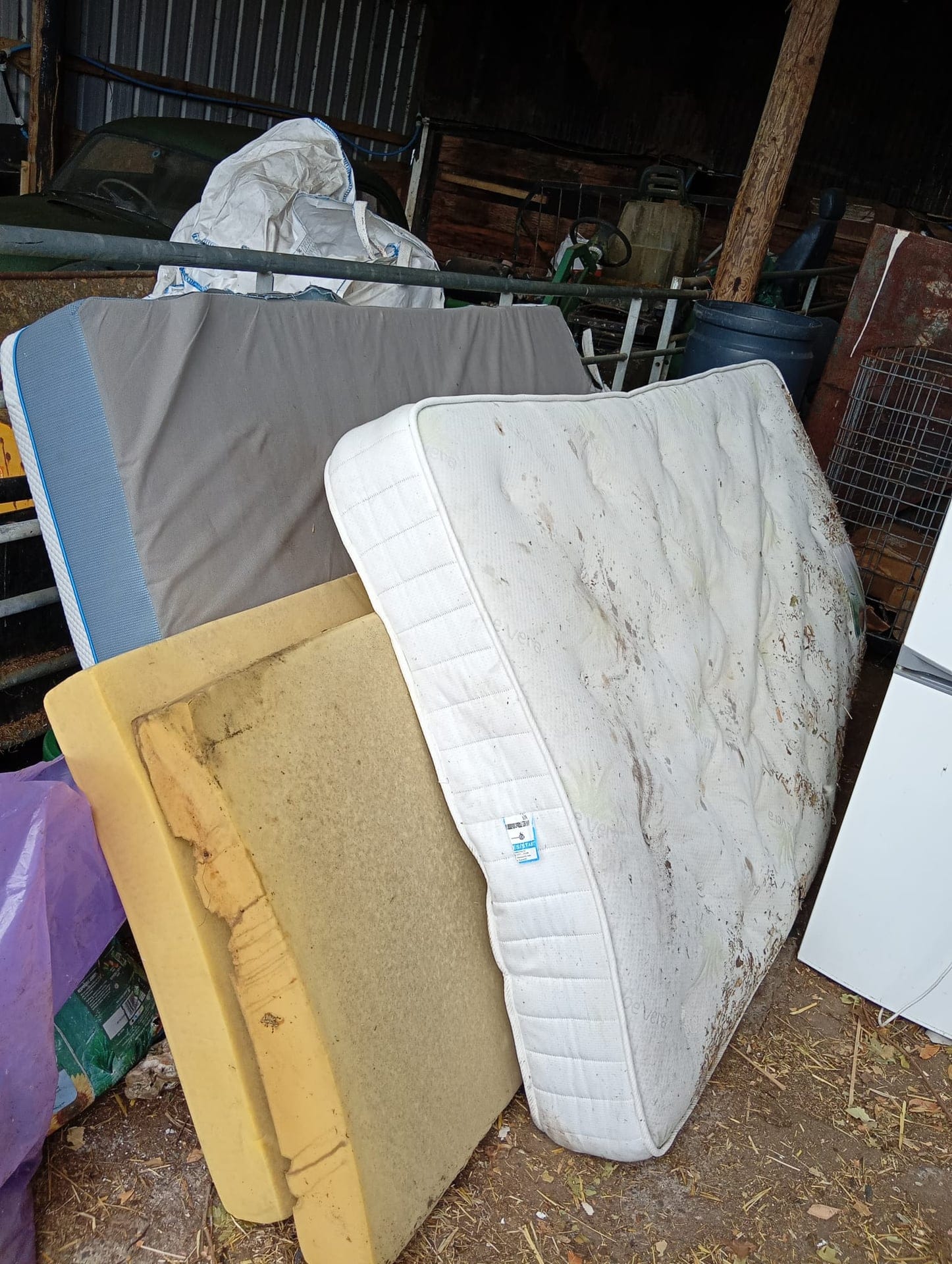 Four old mattresses and a divan base stacked against a barn wall ready for disposal