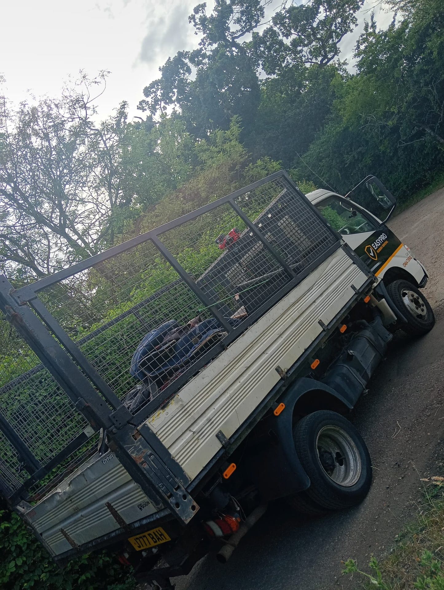 The EasyPro caged tipper truck parked on a tree-lined lane, cage sides up and bed empty